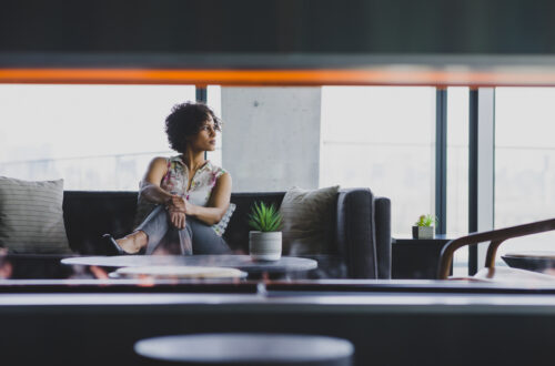 Afro-Latina girl sitting on couch looking to the left with a fireplace in a condo