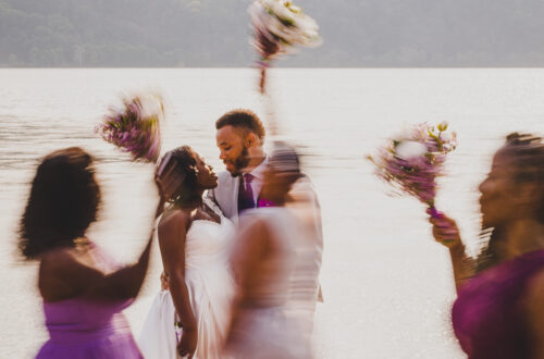 Bride and Groom kissing near a lake in upstate ny in Poughkeepsie with wedding party walking in a blur