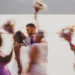 Bride and Groom kissing near a lake in upstate ny in Poughkeepsie with wedding party walking in a blur