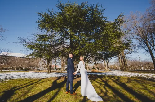 polish couple holding hands walking towards a tree in a park with snow surrounding them