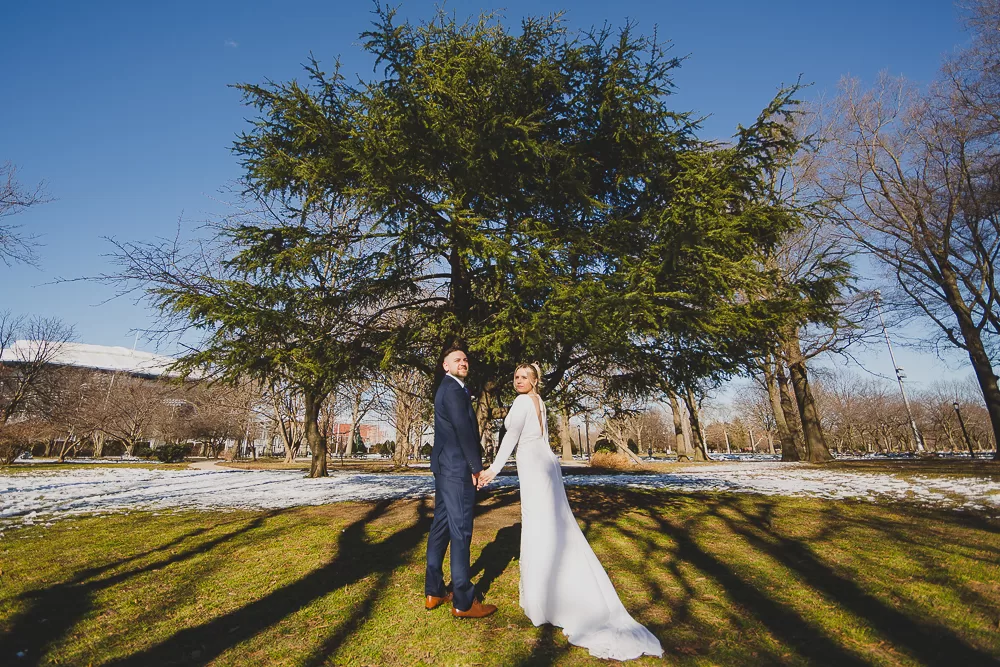 polish couple holding hands walking towards a tree in a park with snow surrounding them