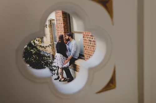 Two people embracing in the foreground. In the background is a round architectural peephole.