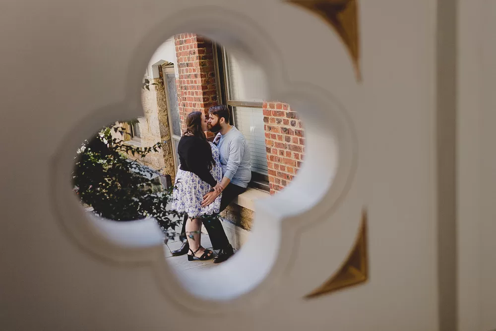 Two people embracing in the foreground. In the background is a round architectural peephole.