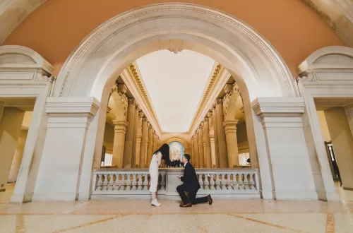 Asian couple proposing on the grand stairs at the MET under a stone arch