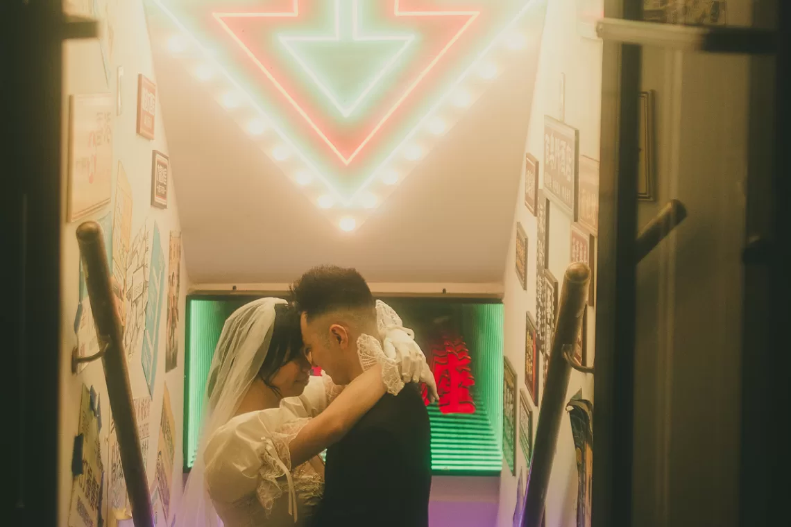 Couple hugging each other in a stairwell with a neon sign arrow pointing at them