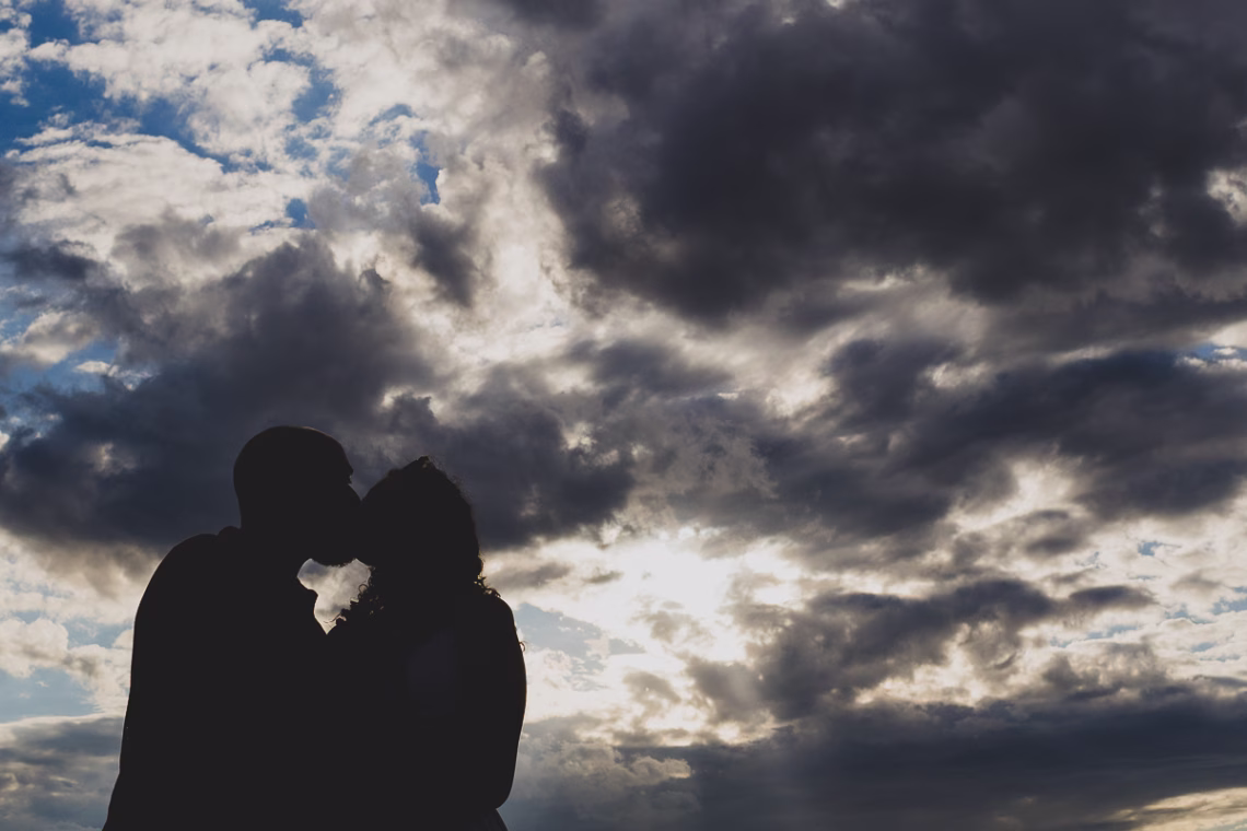 Silhouette of a couple with the sky of dynamic clouds with the sun behind piercing with light