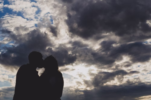 Silhouette of a couple with the sky of dynamic clouds with the sun behind piercing with light