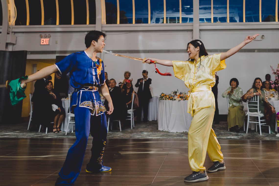 Chinese couple in traditional Wushu attire performing choreographed battle with swords in front of their guests.