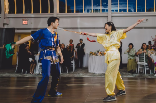 Chinese couple in traditional Wushu attire performing choreographed battle with swords in front of their guests.